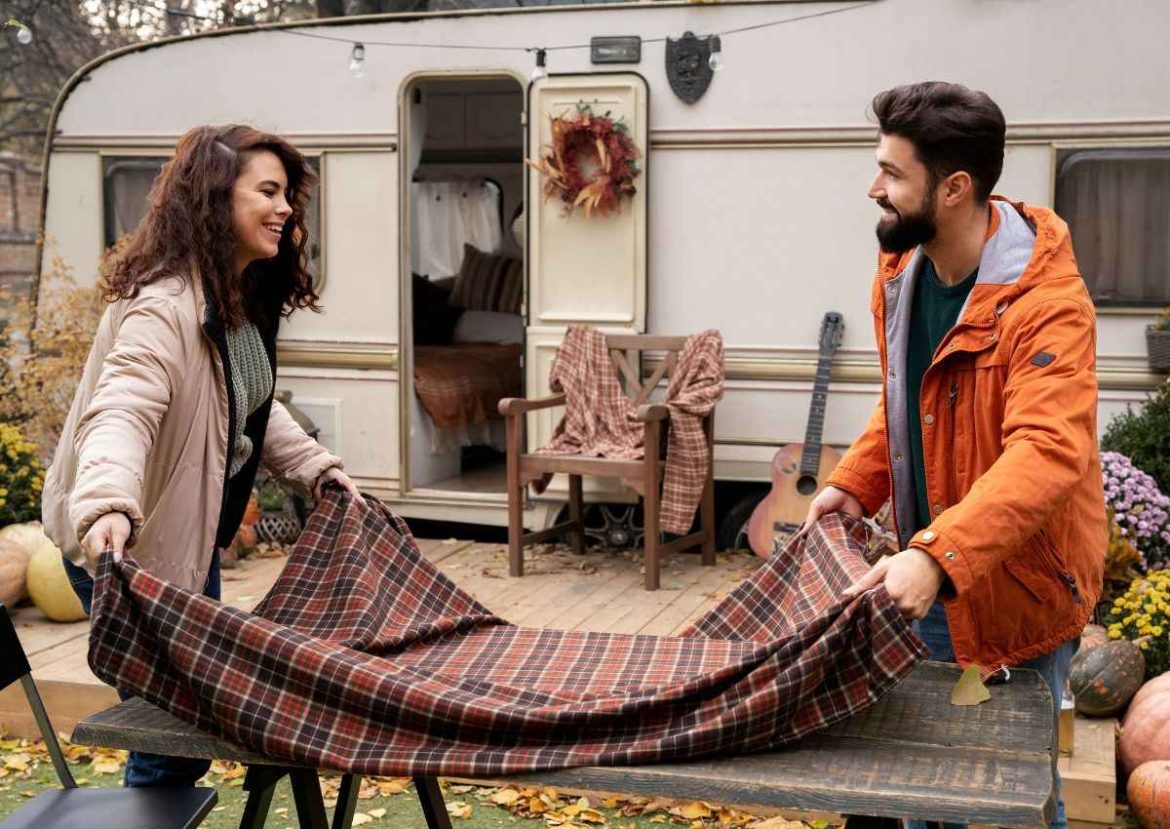 Couple souriant arrangeant une nappe à l'extérieur de leur camping-car en automne.