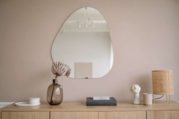 Commode en bois clair avec miroir asymétrique, vase en verre fumé et objets minimalistes illustrant un style de décoration scandinave épuré et naturel.