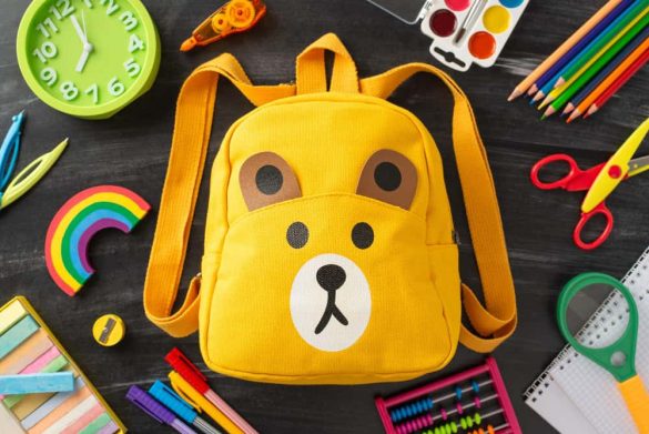 etit sac à dos jaune en forme d'ours entouré de fournitures scolaires, une alternative idéale au traditionnel cartable Super Mario pour la maternelle.