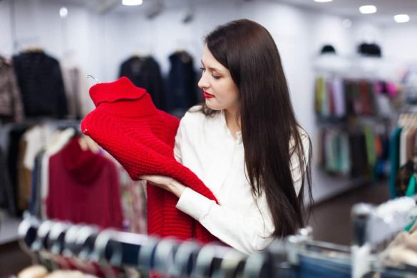 Une jeune femme brune tient un pull rouge en maille dans une friperie à Paris bien éclairée.