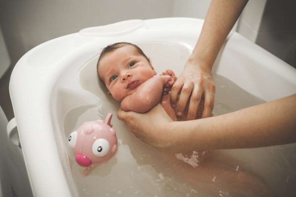 Un petit bébé éveillé prend son tout premier bain, illustrant le quotidien heureux après l'arrivée du premier bébé.