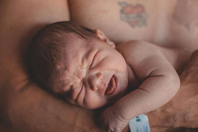 Un nouveau-né emmitouflé dans les bras de ses parents, symbolisant l'émotion intense liée à l'arrivée du premier bébé.